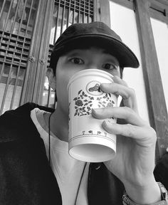 a young man is drinking from a coffee cup while wearing a black hat and jacket