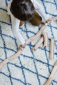 a woman is playing with wooden train tracks on the floor in front of a rug