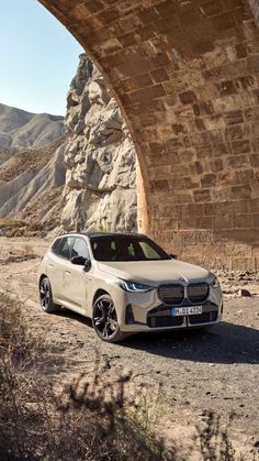 the bmw i3 is parked under an overpass in front of a stone bridge