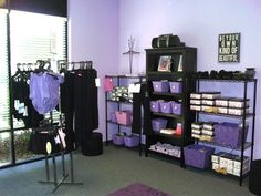 a room with purple walls and black shelvings filled with clothes, bags and other items