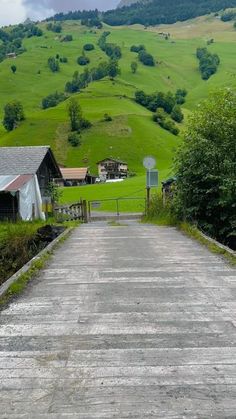 an empty road leading to a farm with green hills in the background