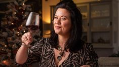 a woman holding a glass of wine in front of a christmas tree