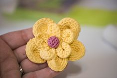 a small yellow crocheted flower with pink center being held by someone's hand