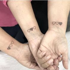 two people holding hands with small hearts on their wrist tattooing each other's wrists