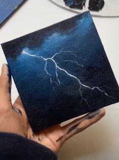 a person holding up a piece of art that has lightning on it and is in their left hand