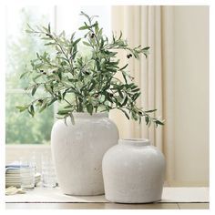 two white vases sitting on top of a table next to each other with plants in them