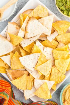 tortilla chips and guacamole on a platter with salsa in the background