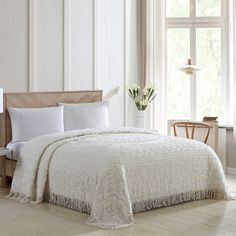 a white bed sitting in a bedroom next to a window with flowers on top of it