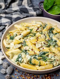 a white bowl filled with pasta and spinach on top of a blue table cloth