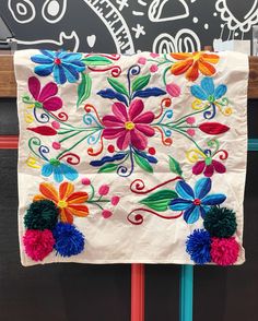 a white wall hanging with colorful flowers and pom poms