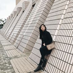 a woman leaning against a wall with her hand on the back of her purse and looking at the camera