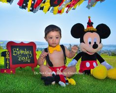 a little boy sitting in the grass next to a mickey mouse and his birthday sign