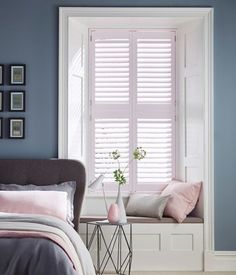 a bedroom with blue walls and white shutters, pink bedding, and a gray headboard