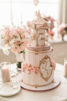 a three tiered cake decorated with pink flowers and gold trimmings on a table