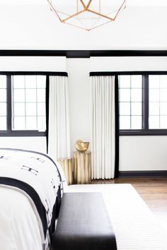 a white bed sitting in a bedroom next to two black and white curtains on the windows