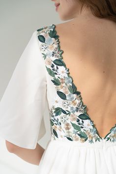 the back of a woman's white dress with flowers on it and green leaves