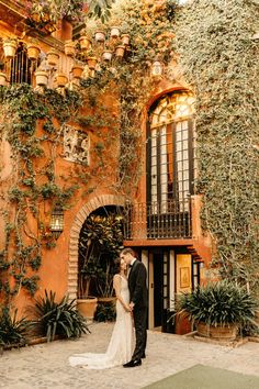 a bride and groom standing in front of an orange building with ivy growing on it