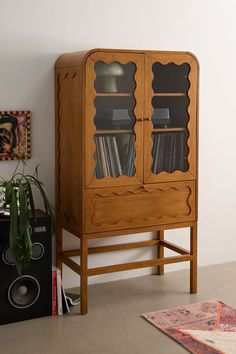 a wooden bookcase with glass doors in the corner next to a rug and speakers