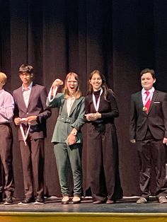 a group of young people standing on top of a stage holding up their hands in the air