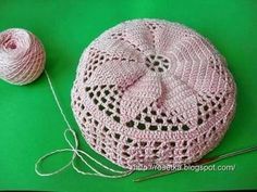 a ball of yarn sitting next to a crocheted hat and knitting needles on a green surface