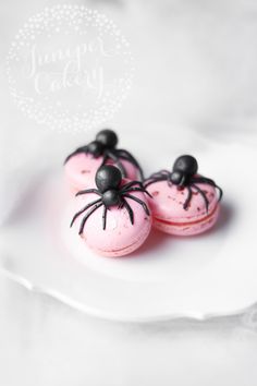 two pink macaroons with black spider decorations on them sitting on a white plate