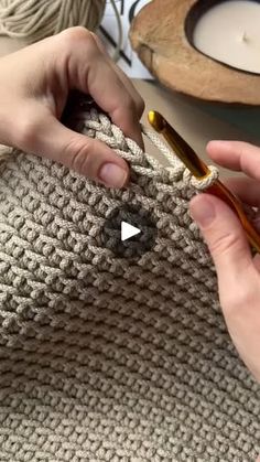 two hands are crocheting the ends of a knitted bag with yarn on it