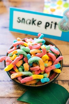 a bowl filled with colorful candy worms next to a sign that says snake pit on it