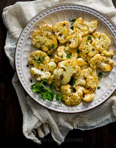 a white plate topped with cauliflower on top of a table next to a napkin