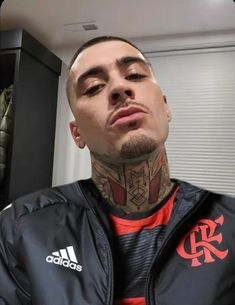 a man with tattoos on his face and chest standing in front of a mirror wearing a black jacket