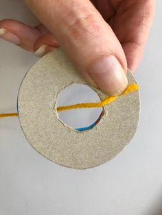 someone is making a hole in the side of a piece of paper with yellow thread