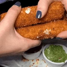 two hands holding fried food in front of some dipping sauces