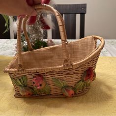 a hand holding a basket with flowers on it sitting on a table next to a christmas tree