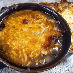 a close up of a bowl of food with bread on the side and another dish in the background