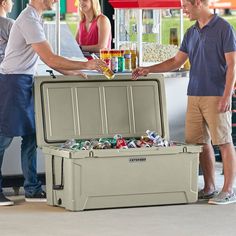 two men standing next to a cooler filled with drinks