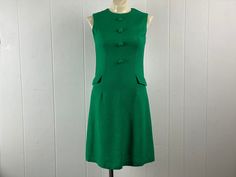 "Vintage 1960s Mod dress. Made of green knit linen or cotton rayon. Has faux button front and two faux hip pockets. Back zipper. Unbranded. About a size small/medium. Actual measurements are:   34\" around the bust  30\" around the waist  34\" around the hips   13.5\" shoulder to shoulder   38\" overall length In very good condition." Vintage Green Dress For Work, Green Knee-length Mod Dress, Green Mod Knee-length Dress, Retro Green Dress With Buttons, Green Mod Cotton Dress, 70s Mode, 1960s Mod Dress, Vintage Dress 60s, 60s And 70s Fashion