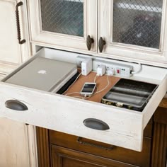 an open drawer in the middle of a desk with electronics and cords attached to it