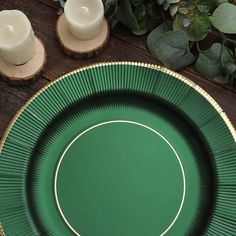 a green and gold plate sitting on top of a wooden table next to two candles