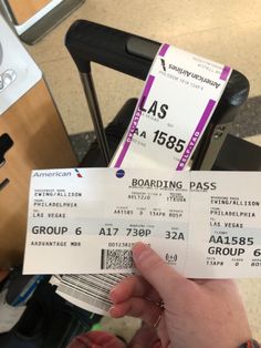 two tickets are held up in front of a person's hand at an airport