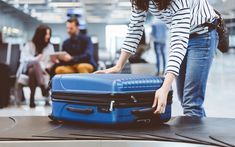 a woman standing over a blue suitcase in an airport