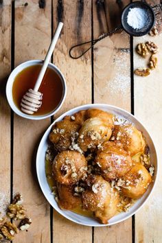 a white bowl filled with cinnamon rolls next to a cup of tea and honey on top of a wooden table