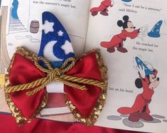 an open book with a red bow and mickey mouse on it's front cover