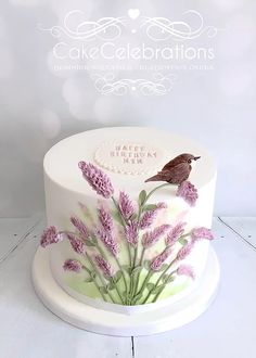 a birthday cake decorated with lavender flowers and a bird on top is shown in front of a white background