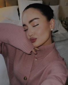 a woman laying on top of a bed wearing a pink sweater and pearl necklaces