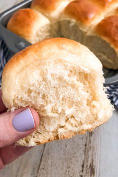 a hand holding a piece of bread in front of a loaf of bread on a plate