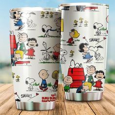 two stainless steel tumblers with cartoon characters on them sitting on a wooden table in front of a blue sky