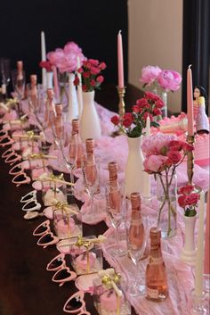 a long table with pink flowers and wine bottles on it, along with candles in vases