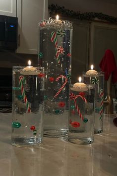 Orbeez Christmas vase with floating candles on top. Inside the four vases the decorations appear to float due to clear orbeez decor. There are candy canes and green and red ornaments in the vases for a Christmas centerpiece. Orbeez Christmas Decor, Floating Candles Christmas, Unique Christmas Decorations Diy, Diy Orbeez, Christmas Floating Candles, Water Beads Centerpiece, Diy Christmas Vases, Floating Candle Centerpieces Diy, Floating Candle Decorations