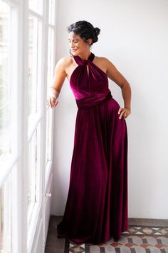 a woman in a purple dress leaning against a window sill with her hands on her hips