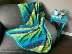 a blue and green crocheted blanket sitting on top of a couch next to a table