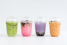 four different colored drinks in plastic cups on a white surface, one is filled with ice cream and the other has chocolate chips